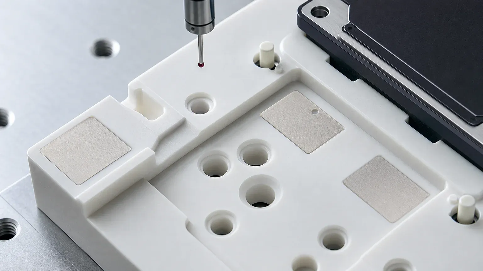 Macro inspection view of alumina ceramic fixture datum pads, locating bores, support lands, and CMM probe for SiC power module assembly